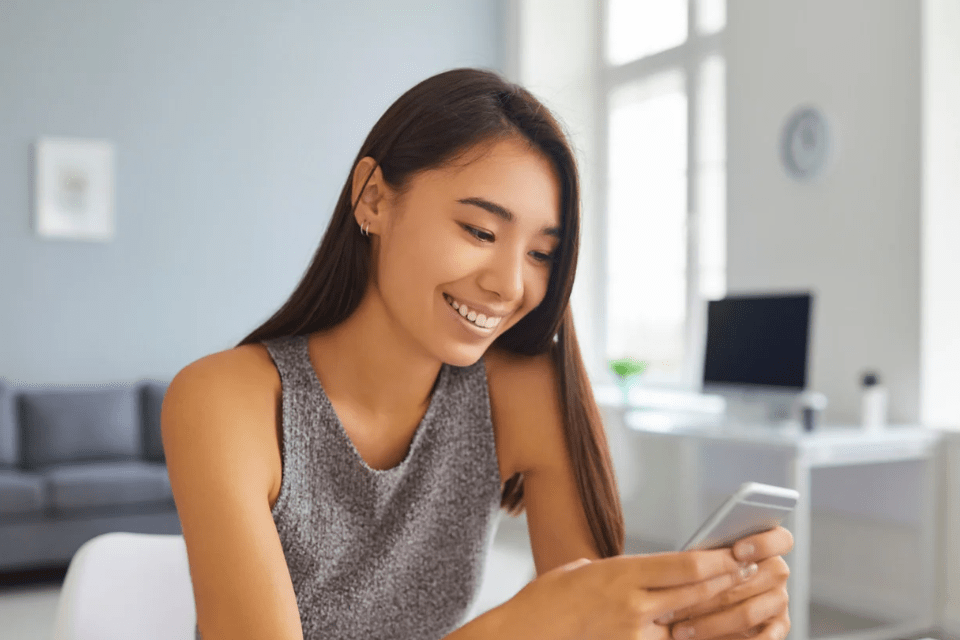 Attractive Smiling Affluent Filipina Millennial Using Her Smart Phone