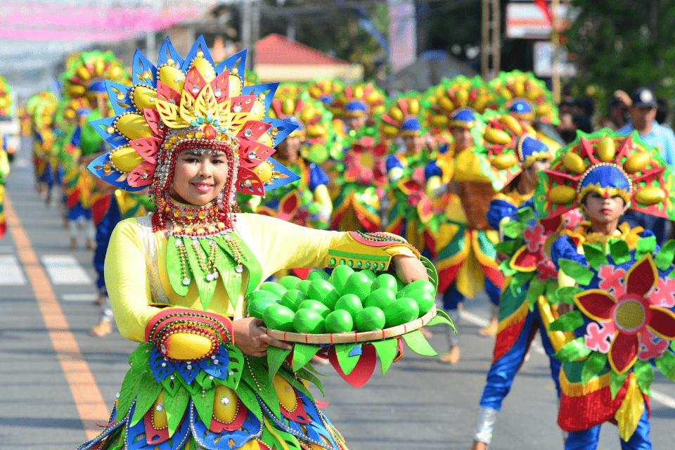 Filipino Woman in Green and Yellow Long Sleeve Shirt Holding a Round Tray of Green Fruit During Sinulog - Effective Communication Tips for Interacting with Filipino Women - Blossoms Dating Blog