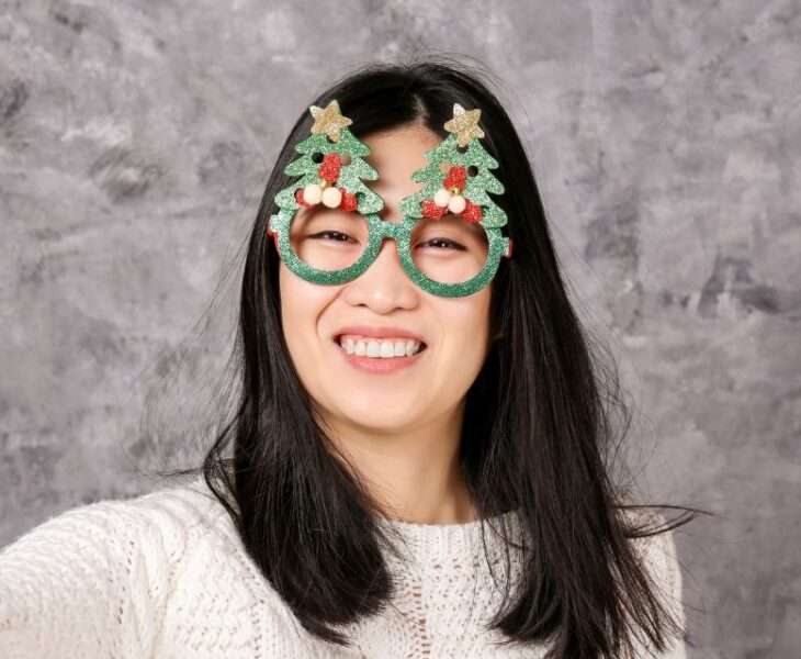A Filipina woman wearing festive Christmas eyewear and smiling brightly.