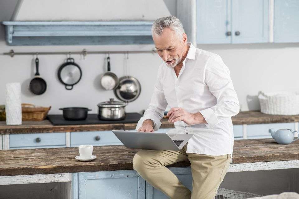 Mature Man in His Kitchen Using His Laptop